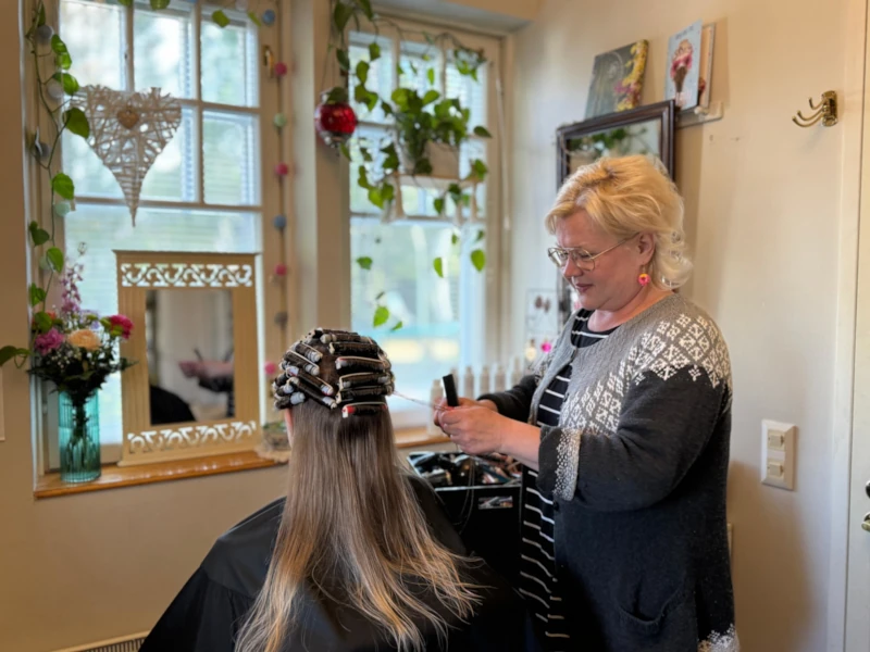 Sannan Salongin kampaaja tekee permanenttia pitkähiuksiselle naisasiakkaalle.